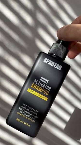 Hand holding a Spartan Root Activator Shampoo bottle in natural light